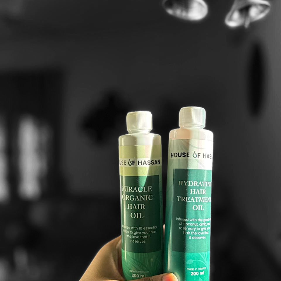 Two bottles of 'House of Hassan's' hair oil products held in front of a mirror.

