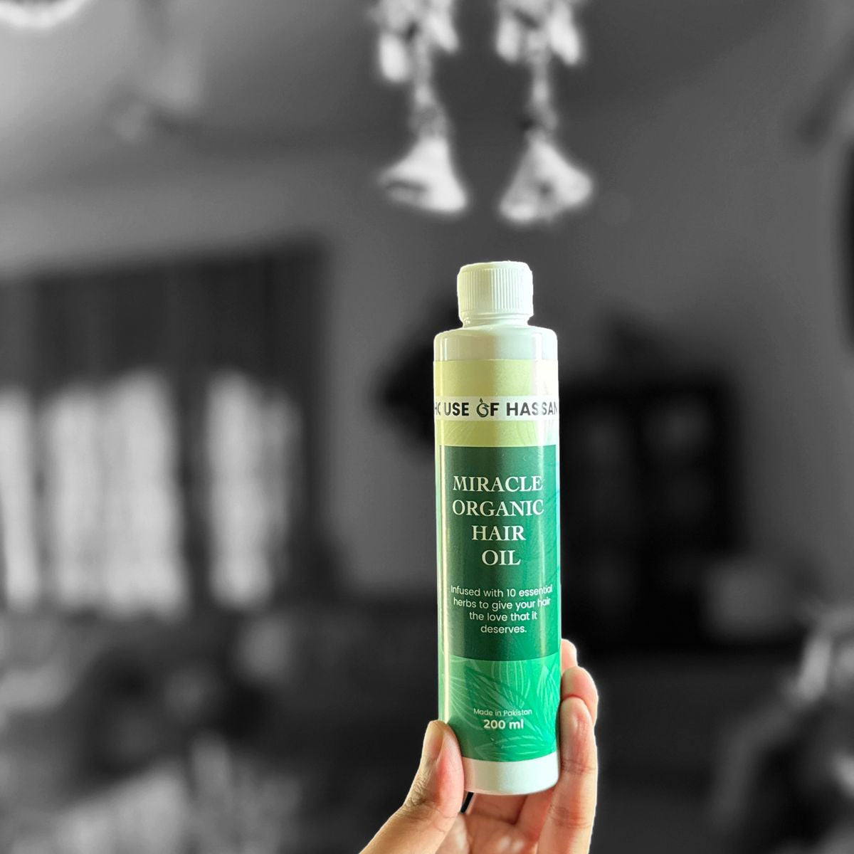 Hand holding a bottle of 'Miracle Organic Hair Oil' with a blurred background


